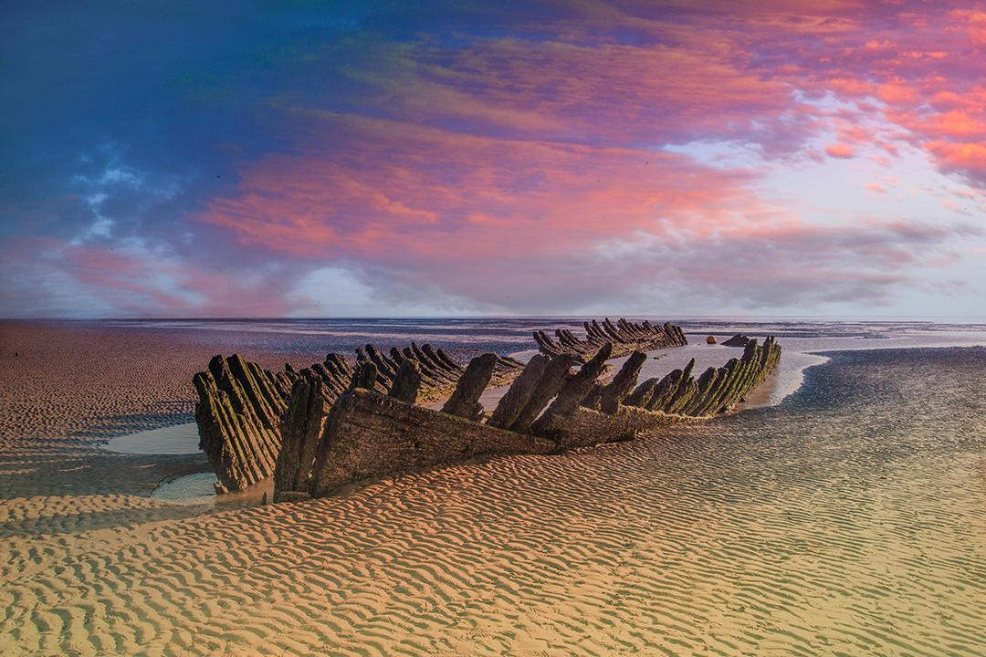 A shipwreck in the sand at sunset